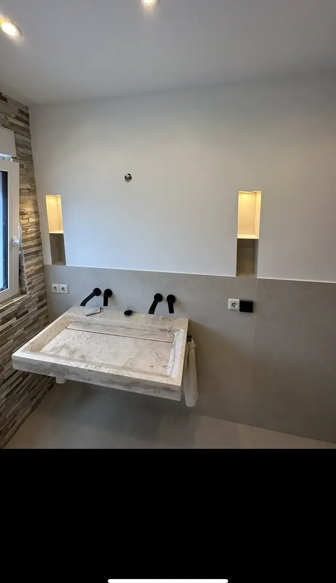 Waschtisch aus Travertin mit Rinnenbecken vor einer Wand aus Natursteinriemchen