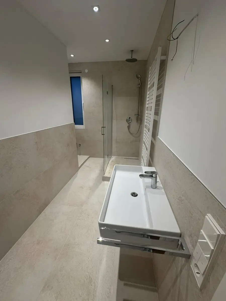 Fertiges Bad in Travertinoptik mit bodengleicher Dusche und wandhängendem Waschbecken